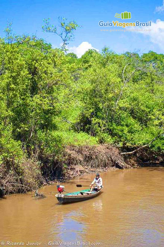 Imagem de pescador em um pequeno barco próximo as margens.